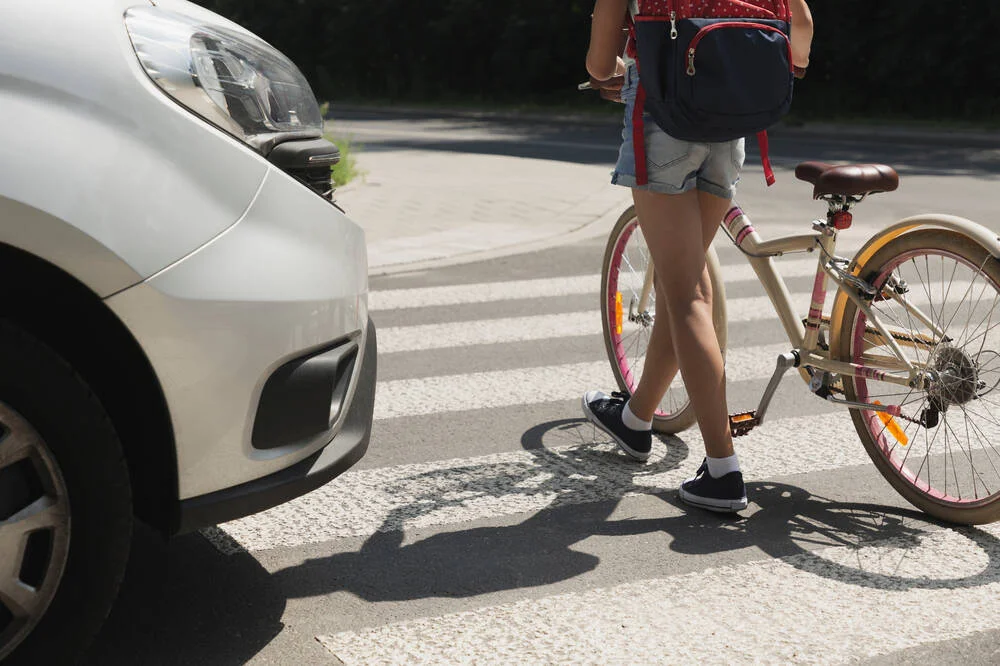 Teenager school girl with backpack and bike walk in pedestrian crossing in front of a car