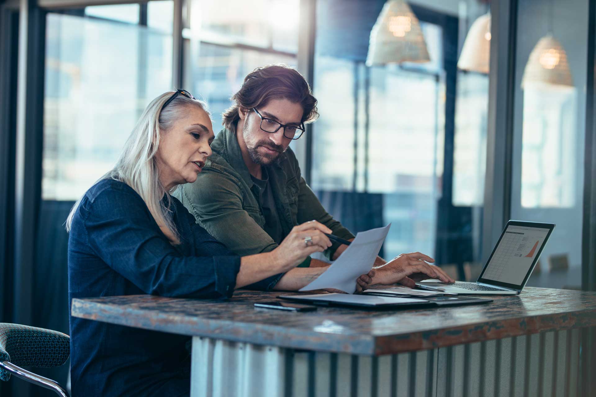 Senior woman discussing work with male colleague. Two business associates working together in office and talking over a business report.