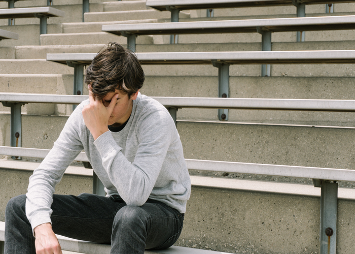 Depressed teen sitting alone on bleachers.