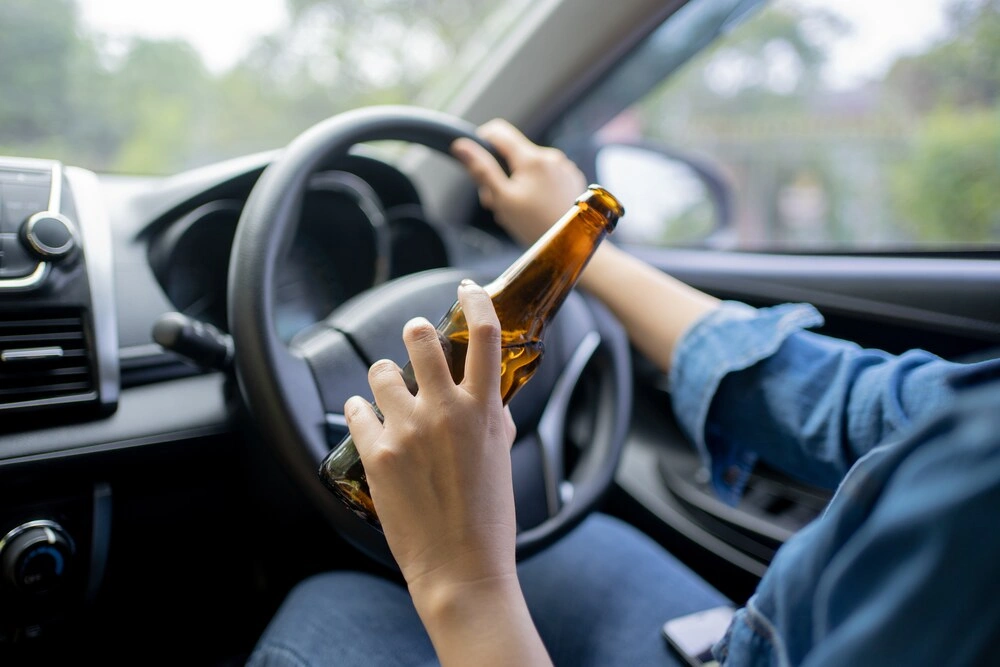 Hand holding alcoholic bottle while driving