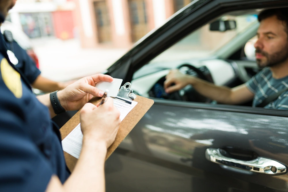 Close up of a police cop writing a traffic ticket or fine to a male driver in his car for speeding